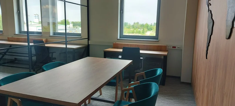 A meeting table with turquoise chairs and a desk by the window.