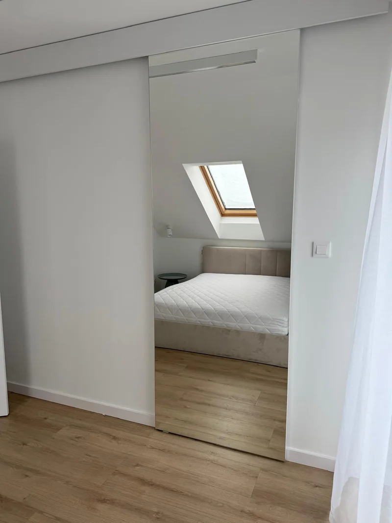 Mirror reflecting the bedroom beneath a sloping ceiling.