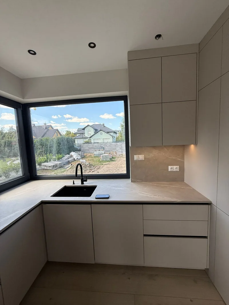 A black sink and tap against the background of a light countertop by the corner window.