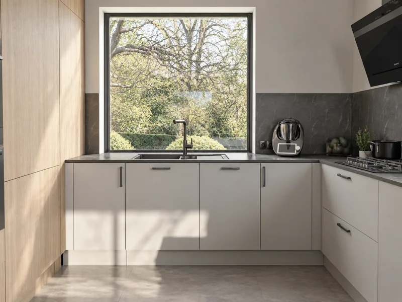 Bright fronts, grey countertop and sink under a large window.